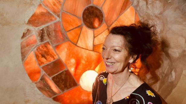 Eine Frau mit lockigen, roten Haaren vor orangenem Glasfenster 