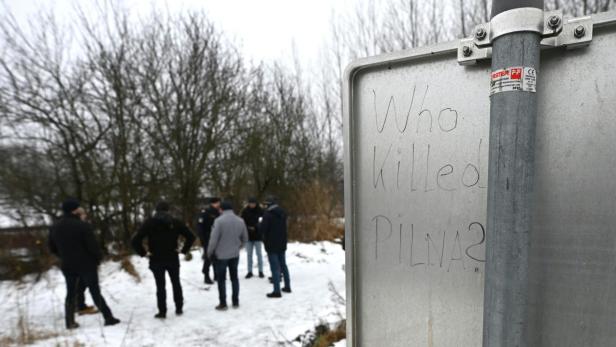 Who killed Pilna? steht auf einem Schild, dahinter stehen Leute