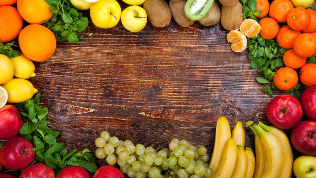 Verschiedene frische Obstsorten wie Äpfel, Bananen, Trauben und Zitrusfrüchte auf Holztisch.