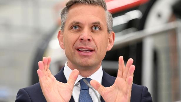 Ein Mann im Anzug spricht und gestikuliert mit beiden Händen, im Hintergrund unscharfe technische Umgebung.