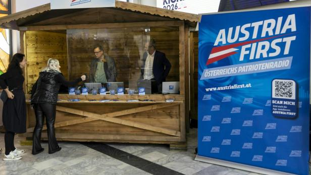 Der Stand des Senders Austria First beim Neujahrstreffen der FPÖ 2026 in Kärnten. Zu sehen sind zwei Personen in einer Hütte, hinter einer Glaswand.