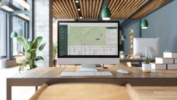 Monitor mit Fuhrparkmanagement-Software und Kartenansicht in modernem Büro mit Pflanzen.