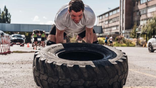 Mann hebt im Freien einen großen Traktorreifen bei einem Fitness-Training an.