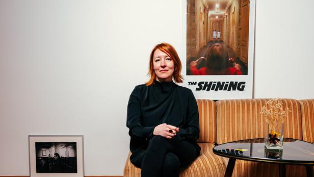 Barbara Kaufmann sitzt auf einem Sofa, hinter ihr ein Filmposter von The Shining
