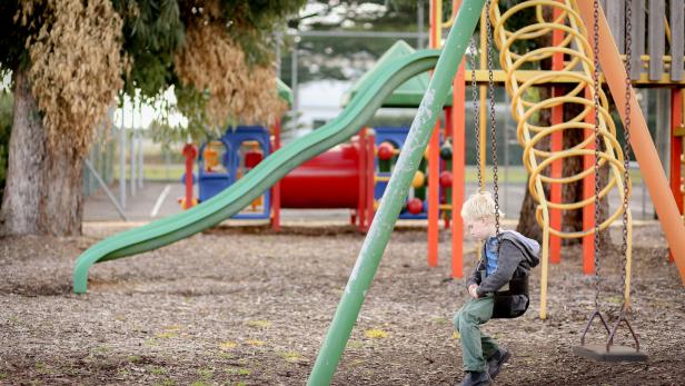Ein Kind sitzt allein auf einer Schaukel am Spielplatz.