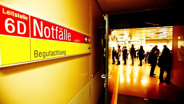 Ein Flur mit einem Notfall-Schild und mehreren wartenden Menschen in einem hell beleuchteten Bereich.