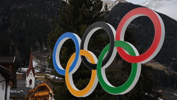 Eine plastische Darstellung der Olympischen Ringe, installiert vor einem Dorfpanorama in Italien