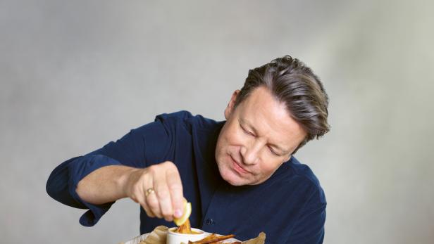 Jamie Oliver blickt auf einen Teller mit Erbsen und paniertem Fisch.