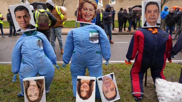 Mercosur-Protestierende stehen in Warnwesten und mit Schildern auf einer Straße. Im Vordergrund sind drei ausgestopfte blaue Ganzkörper-Anzüge zu sehen. Dort wo der Kopf rausschauen sollte, hängen stattdessen Bilder der am Abkommen beteiligten Staatsoberhäupter. Links Santiago Peña, Mitte Ursula von der Leyen, rechts Brasiliens Ex-Präsident Jair Bolsonaro