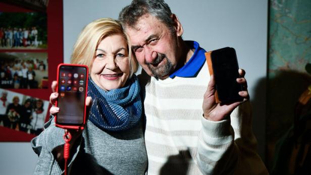 Ein Pensionistepaar steht zusammen, beide halten ihre Handys hoch