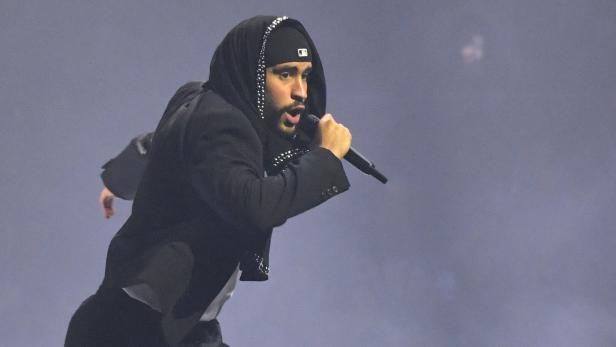 Der Musiker Bad Bunny singt in schwarzem Outfit bei einem Auftritt in sein Mikrofon.