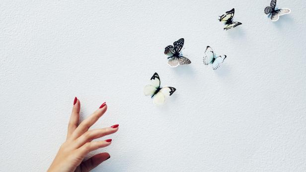 Schmetterlinge fliehen vor einer Hand, die sie zu fassen sucht 