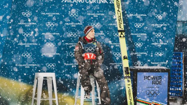 Der Skispringer Jan Hörl sitzt vor einer Werbewand auf einem Barhocker in heftigem Schneetreiben