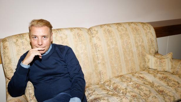 Modedesigner Atil Kutoglu sitzt auf einem gelb-braunen Sofa