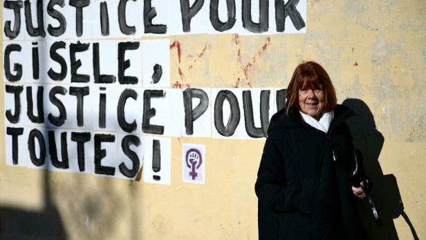 Gisèle Pelicot steht vor einer Mauer, auf der geschrieben steht: „Gerechtigkeit für Gisèle, Gerechtigkeit für alle!