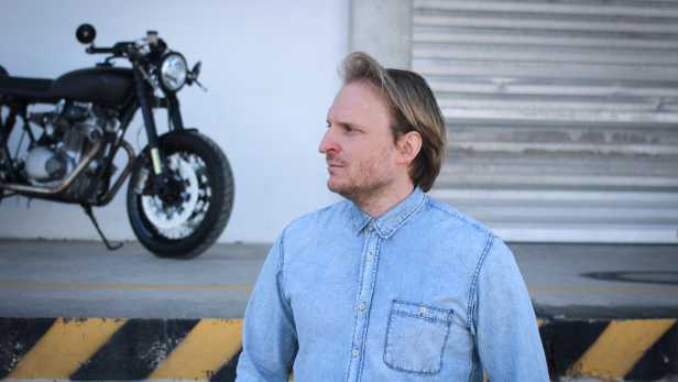 Ein Mann steht in einer Jeansjacke vor einem Motorrad