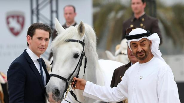 Ein weißes Pferd steht zwischen einem Mann im Anzug und einem Mann in traditioneller arabischer Kleidung.