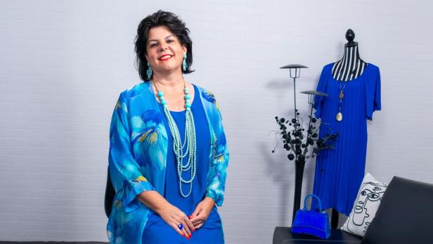 Eine brünette Frau in einem blauen Gewand vor einer weißen Wand