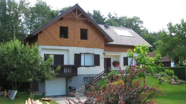 Einfamilienhaus mit Holzfassade, Garten und umgeben von Bäumen an einem sonnigen Tag.