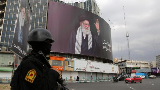 Ein vermummter Soldat mit Waffe steht auf einer Straße in Teheran, im Hintergrund ein großes Bild des Obersten Führers Chamenei