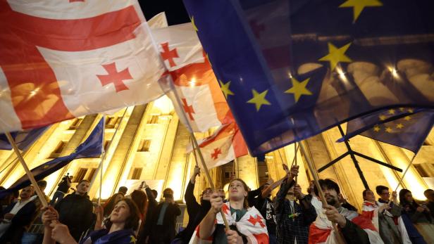 Protestierende schwenken EU- und Georgien-Flaggen vor dem georgischen Parlament im Hintergrund.