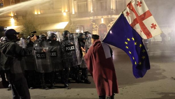 Ein Mann steht mit EU und Georgien-Flagge vor Anti-Riot-Polizisten.