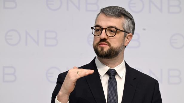 Mann mit Anzug, Bart und Brille vor einer weißen Wand mit OeNB-Logo.