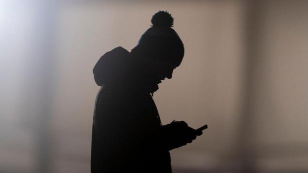 Ein Mann schaut auf ein Smartphone und zeichnet sich als Silhouette ab. 