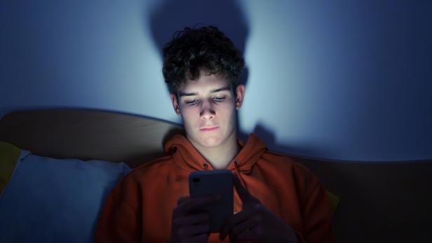 Teenager mit Smartphone liegend im Bett in der Nacht