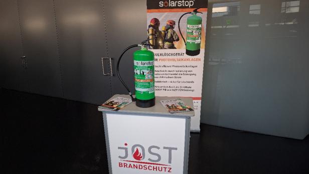 Ein grüner Feuerlöscher auf einem kleinen hohen Tisch vor einer Plakatwand