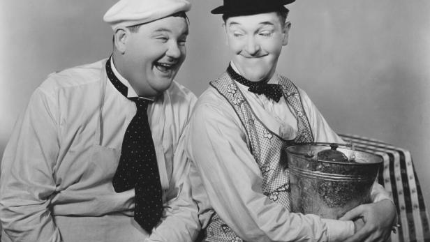 Der Hollywood-Comedian Oliver Hardy lacht seinen ebenfalls fröhlich aussehenden Kollegen Stan Laurel treuherzig an