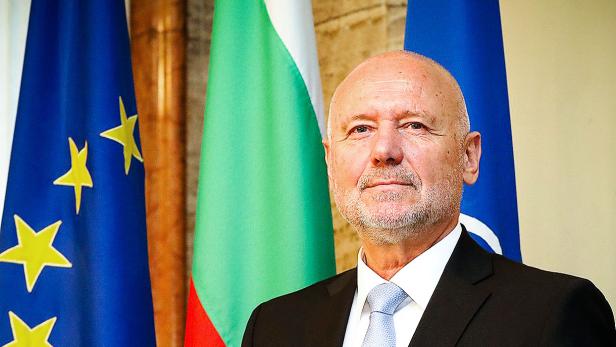 Ein Mann im Anzug steht vor den Flaggen der EU, Bulgariens und der NATO.