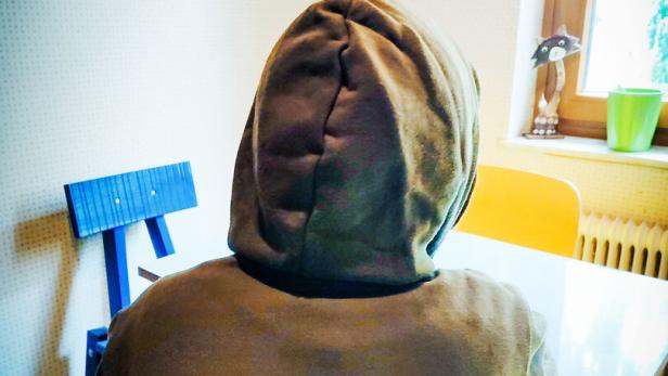 Eine Frau mit Kaputzenpulli sitzt in einer Küche