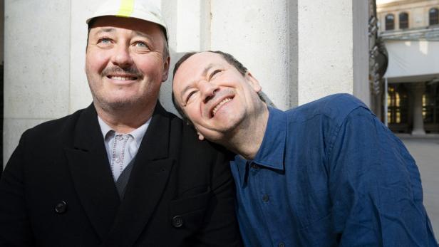 Die beiden Attwenger-Musiker Hans Peter Falkner und Markus Binder lehnen nebeneinander an einer Mauer und lächeln