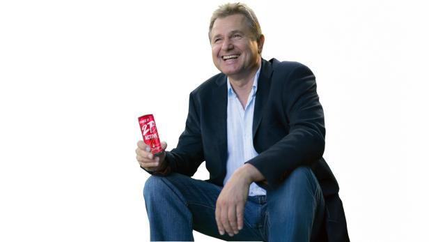 Ein Mann sitzt und hält lächelnd eine Getränkedose in der Hand.