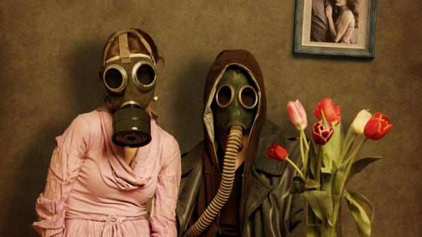 Ein Paar, beide mit Gasmasken, in trostloser häuslicher Atmosphäre.