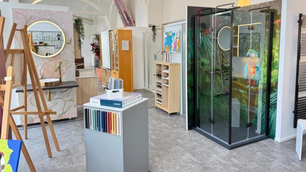 Moderne Badausstellung mit Waschtisch, Farbmusterbox und Duschkabine mit Papageienmotiv.