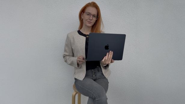 Eine Frau sitzt auf einem Hocker und hält ein Apple-Laptop in den Händen.