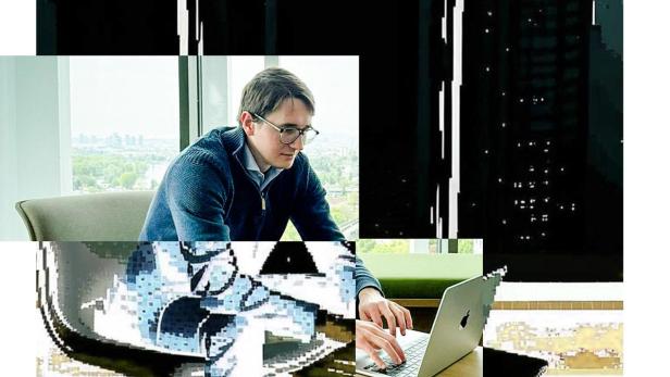 Ein junger Mann sitzt an seinem Laptop und arbeitet. Der Hintergrund ist mit Pixeln verfälscht, um den Einfluss der KI auf die heutige Jobwelt zu symbolisieren.