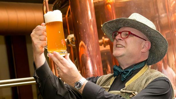 Bierkenner Conrad Seidl mit Hut begutachtet vor einem Braukessel ein frisch gezapftes Bier