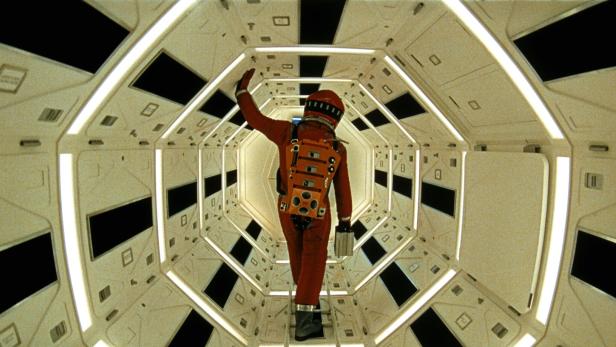 Mann in orangem Raumanzug durchquert einen hellen futuristischen Korridor