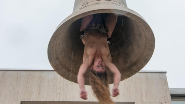 Die nackte Künstlerin Florentina Holzinger hängt kopfüber, als menschlicher Klöppel, in einer großen Messingglocke 