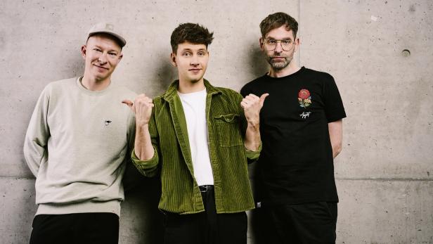 Das Trio Deine Freunde posiert für ein Foto vor kahler Wand