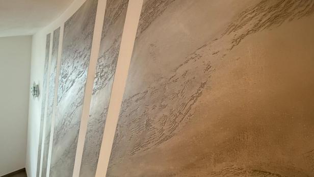 Strukturierte Wand mit abwechselnd glatten und rauen, silbrig glänzenden Streifen in einem Flur.