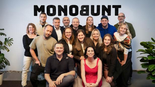 Gruppenfoto von 16 Personen vor einer Wand mit dem Schriftzug „MONOBUNT“.