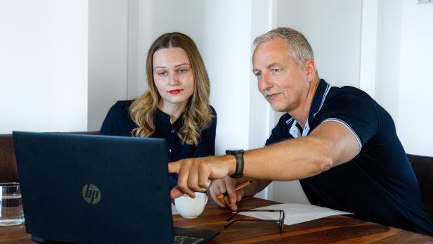 Zwei Personen besprechen gemeinsam Inhalte auf einem Laptop an einem Holztisch.