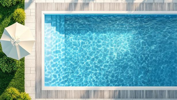 Moderner Pool mit klar blauem Wasser, Holzumrandung und Sonnenschirm im Garten aus der Vogelperspektive.