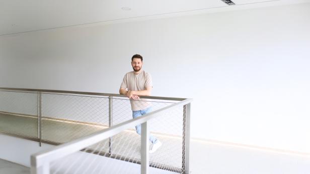 Ein Mann lehnt an einem modernen Geländer in einem hellen, minimalistischen Innenraum.
