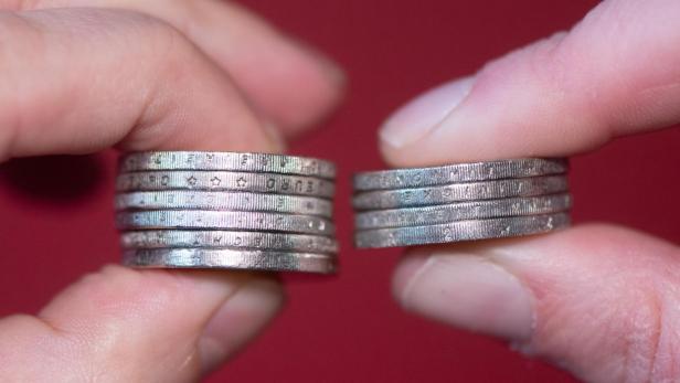 Zwei Hände halten Euro-Münzen zwischen den Fingern.
