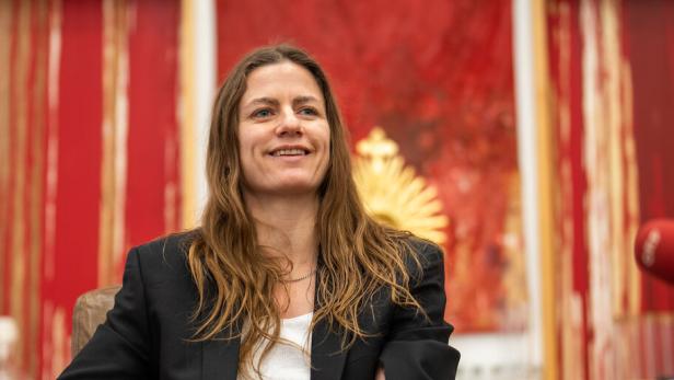 Die Künstlerin Florentina Holzinger lächelt, im Hintergrund Schüttbilder des Aktionisten Hermann Nitsch